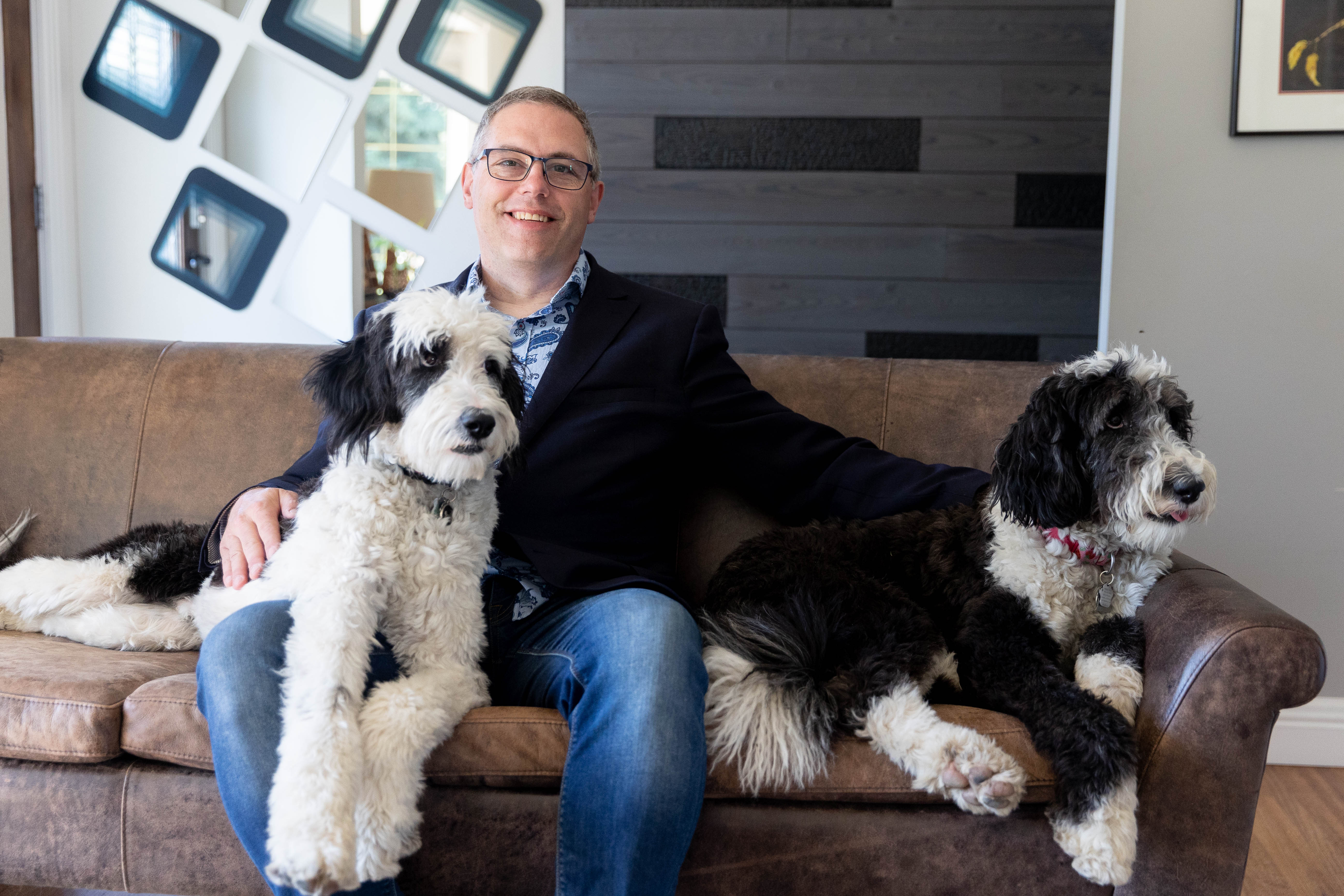 Peter sitting in a couch at home with his sheepadoodles Walter and Maggie