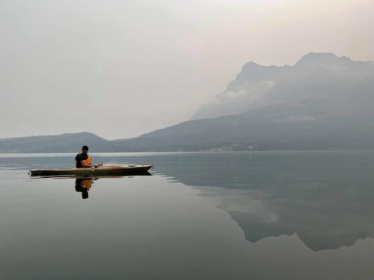 Peter in a kayak on Waterton Lake with a glassy surface reflecting the mountains behoi